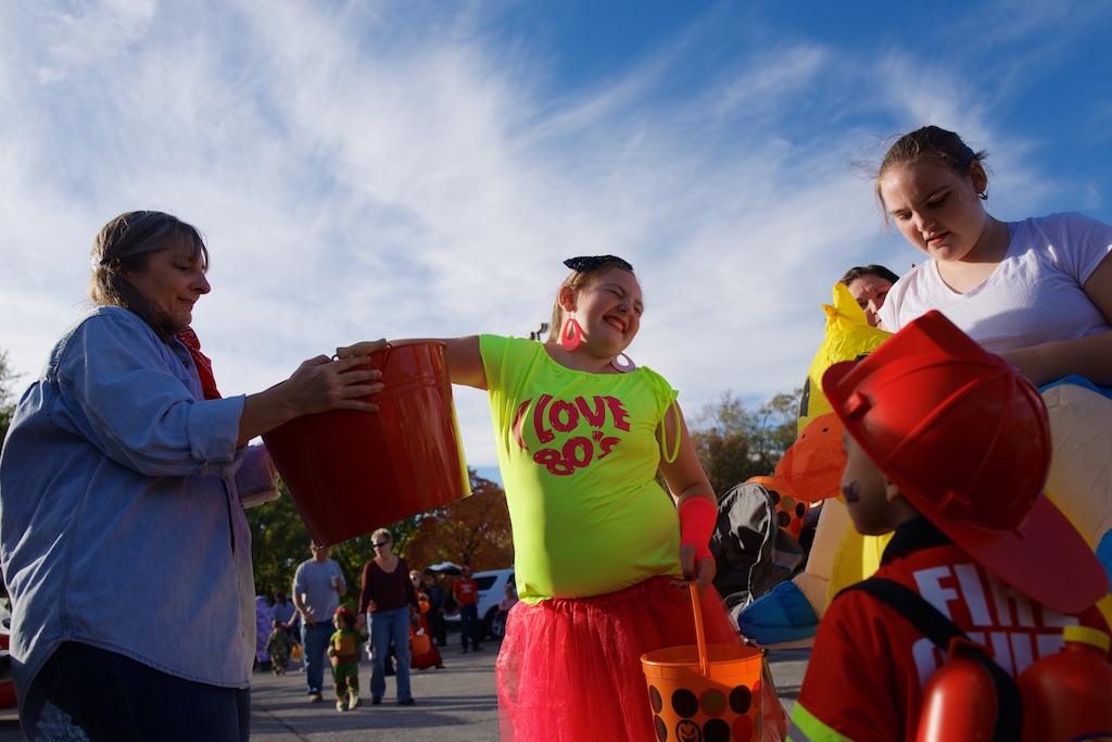 A girl in an "I love the 80s" costume looks away while reaching into a bucket of toys while other costumed children look on.